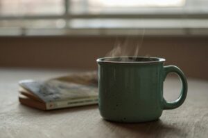 a steaming green mug and worn paperback book resting together on a naturally lit table