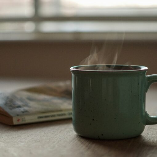 a steaming green mug and worn paperback book resting together on a naturally lit table