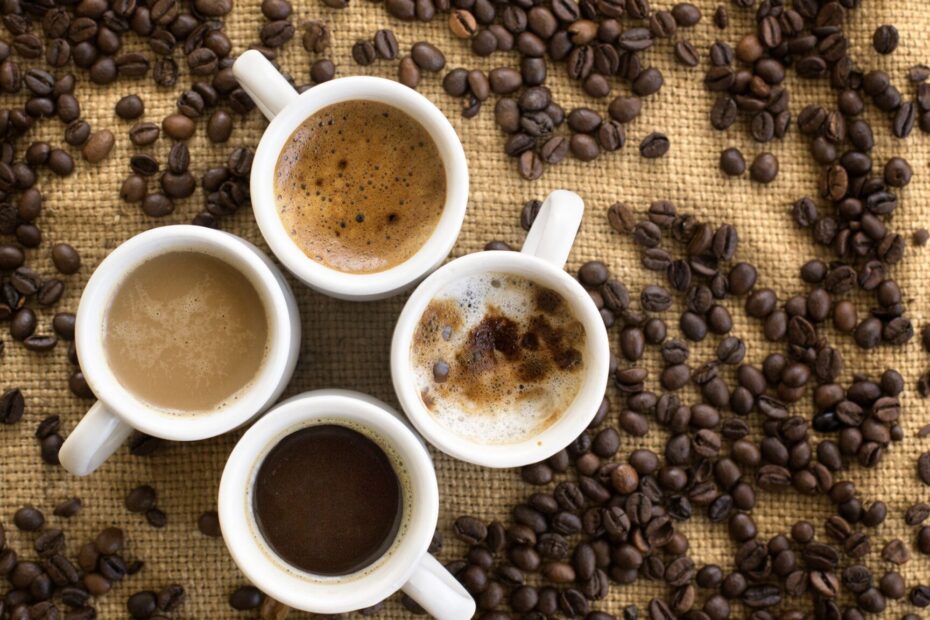 An image of four cups filled with coffee on the background of burlap and coffee beans