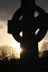 Stone monument of Celtic Cross with low sun in background on horizon